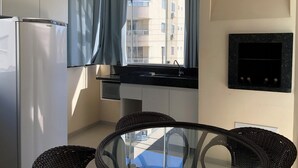 A compact kitchen with a refrigerator, a sink, and a dining area with a glass table and wicker chairs. - Lagoinha Beach Residencial (Bombinhas)