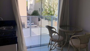 A balcony with wicker chairs, a glass table, and a view of parked cars and buildings. - Lagoinha Beach Residencial (Bombinhas)