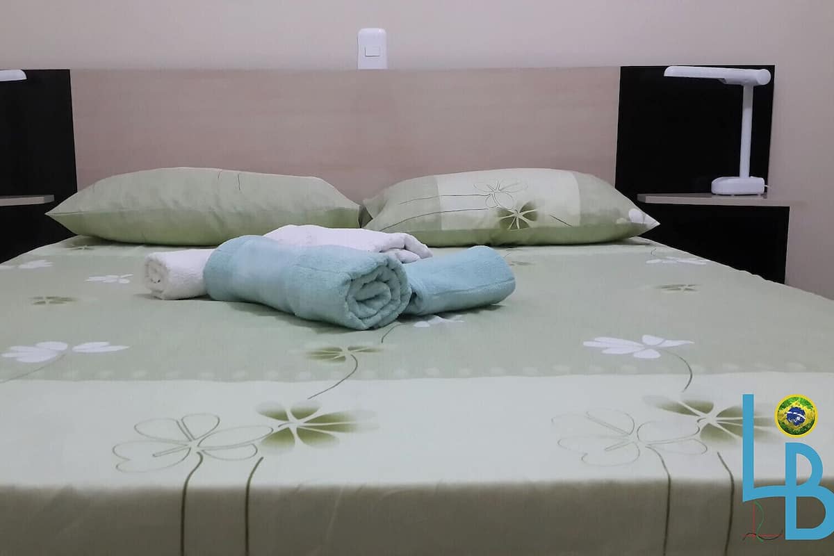 A neatly made bed with a floral bedspread, two pillows, and two rolled towels.