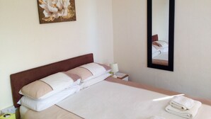 A neatly made bed with a headboard, a bedside lamp, a mirror, and a floral artwork on the wall. - Arlingtons (Blackpool)