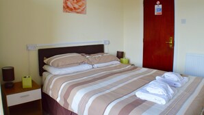 A neatly made bed with striped bedding, a bedside table with a lamp, a nightstand, and a red door with a sign. - Arlingtons (Blackpool)