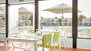 Une chambre d’hôtel avec vue sur la piscine, une table en verre et des chaises vertes.