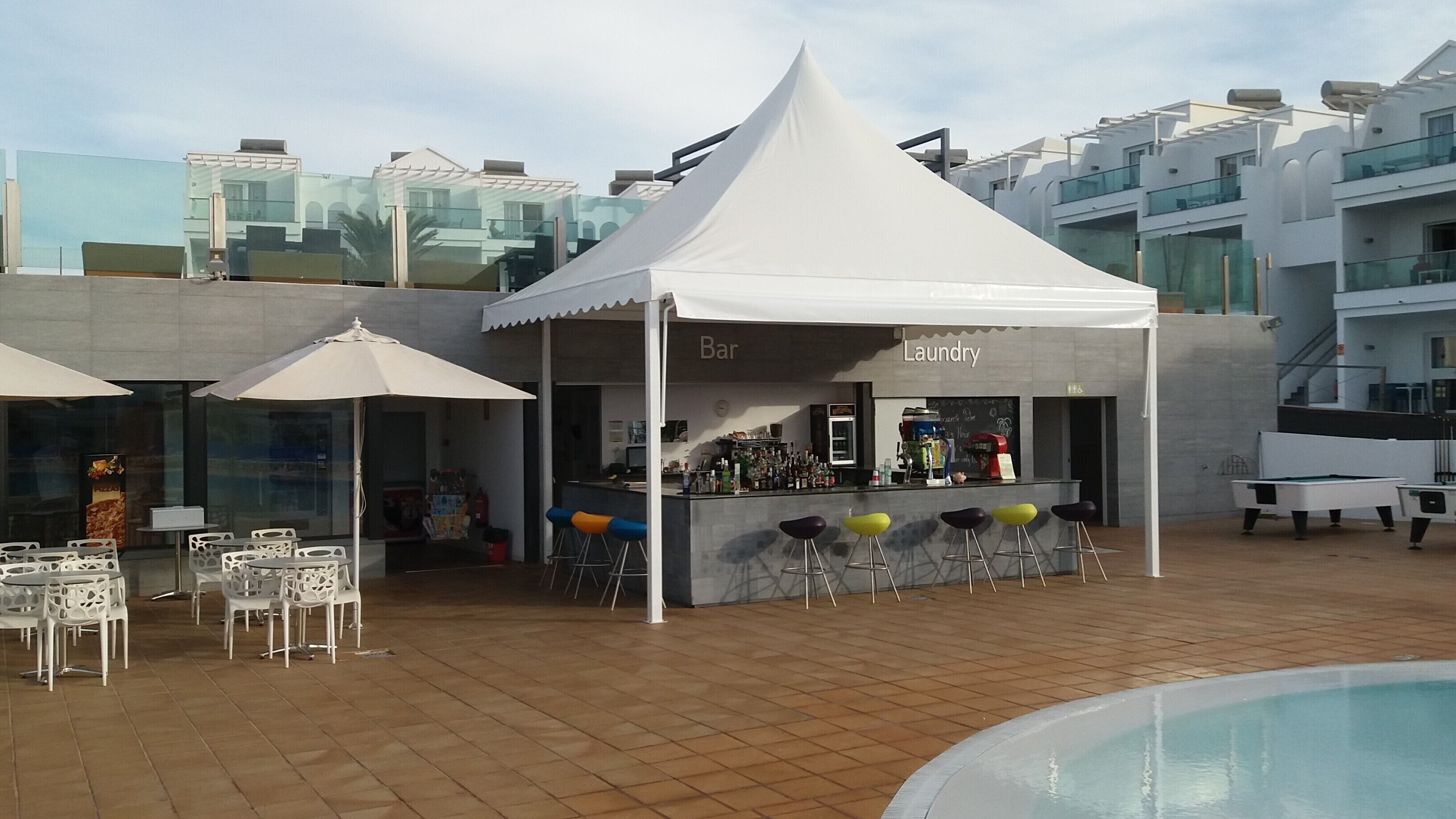 Eine Dachterrasse mit weißem Baldachin, Barhocker und einem Billardtisch.