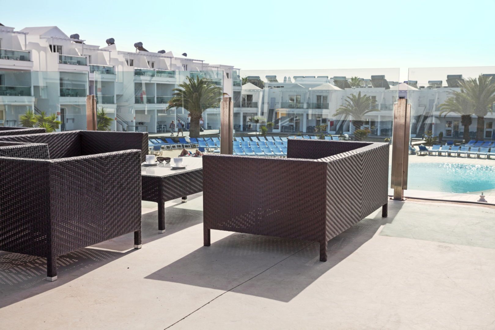 A rooftop terrace with wicker furniture, a pool, and a view of modern buildings.