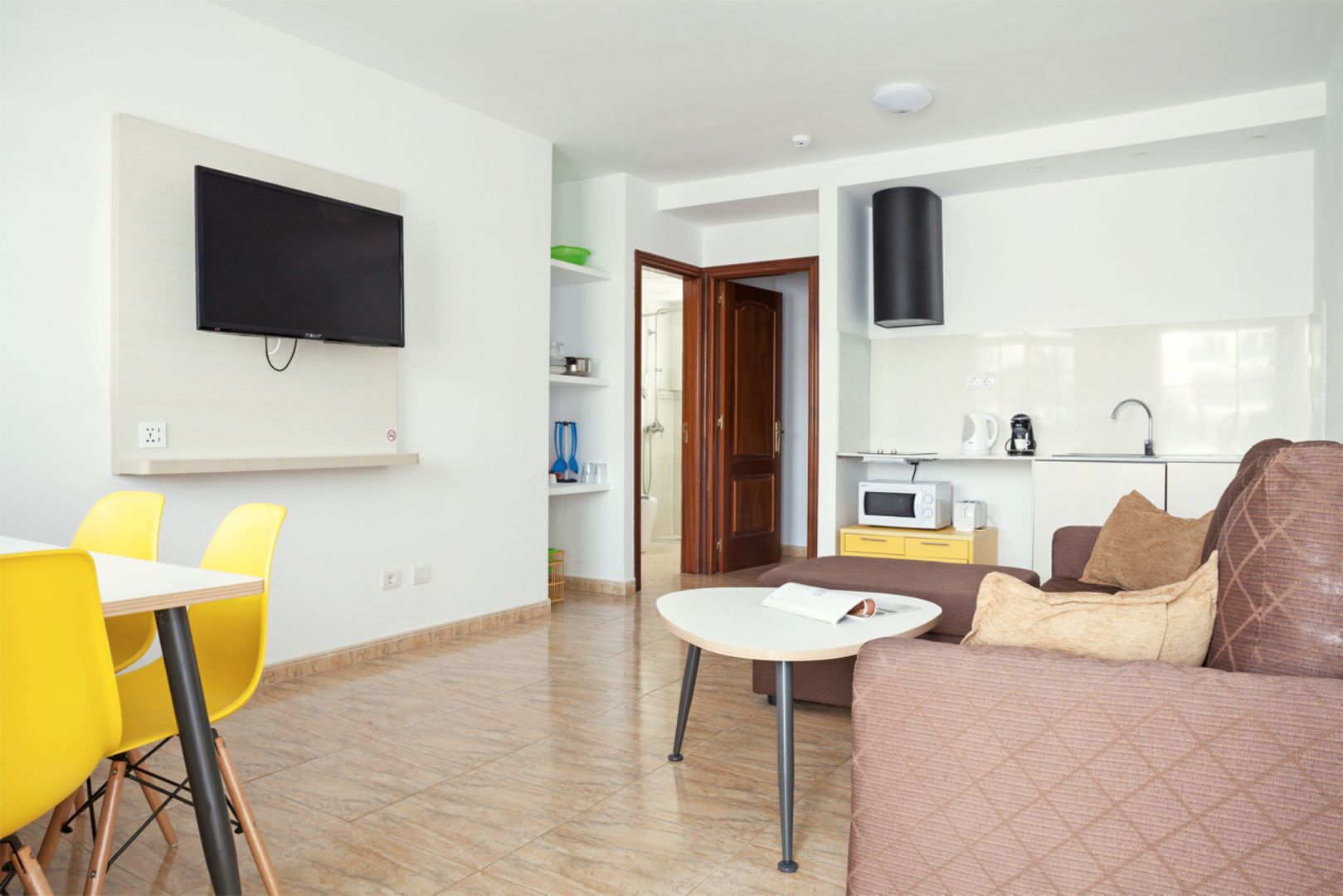 Una sala de estar moderna con una televisión de pantalla plana, sillas amarillas, un sofá marrón y una mesita blanca.