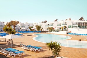 A pool area with blue lounge chairs and umbrellas, surrounded by white buildings with balconies.