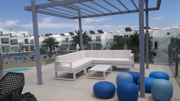A rooftop lounge area with a white sectional sofa, a small table, and blue exercise balls.