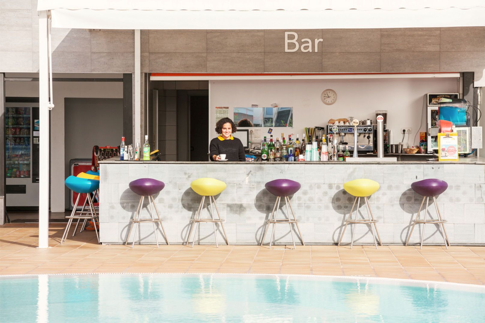 A bar with a poolside view, featuring a bar counter, stools, and a pool.