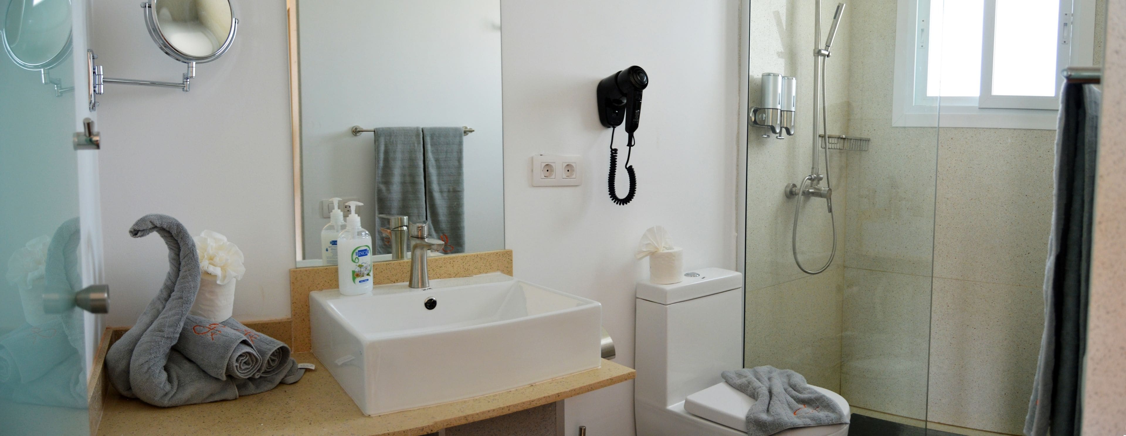 A bathroom with a white sink, a mirror, a towel, a hairdryer, and a shower.