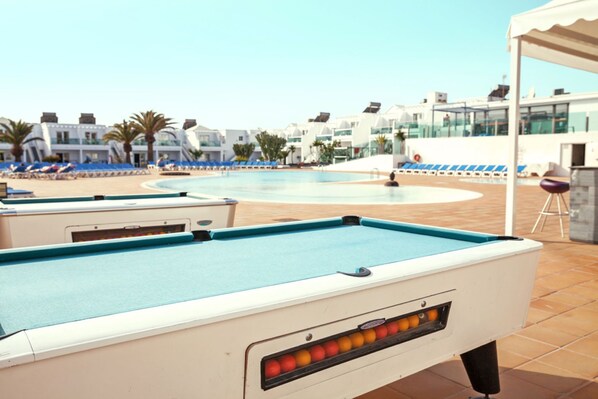 A pool table in a resort setting with a pool and lounge chairs in the background.