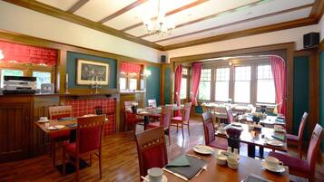 A restaurant with wooden floors, red chairs, and a large window with curtains.