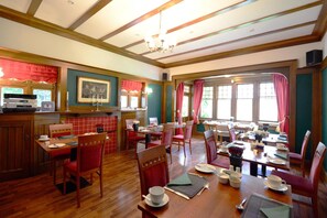 A restaurant with wooden floors, red chairs, and a large window with curtains.
