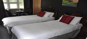 Habitació d'hotel amb dos llits individuals, una taula petita amb una paperera, una cadira i una finestra amb cortines.