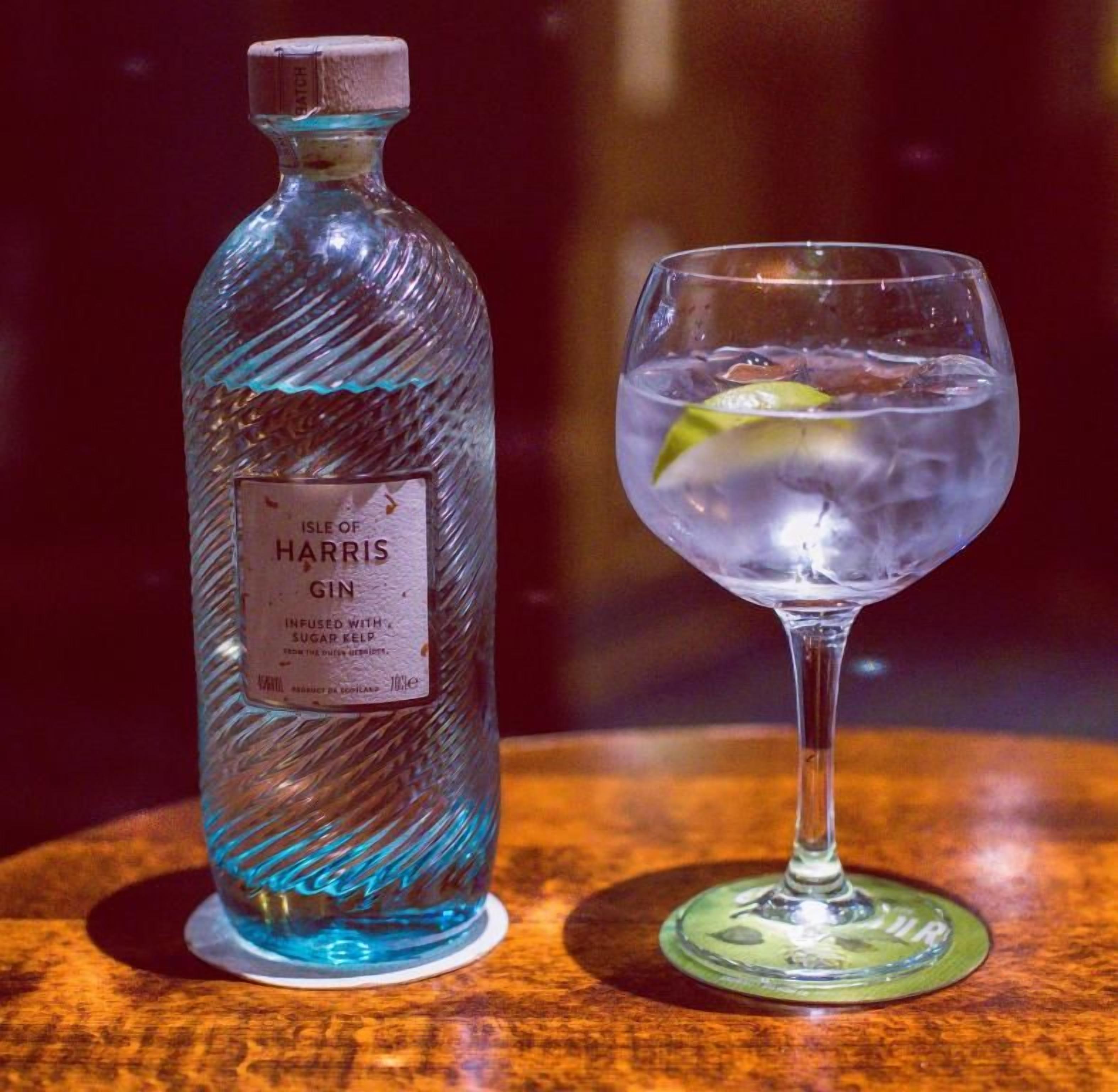 A bottle of gin and a glass with a lime wedge on a wooden surface.