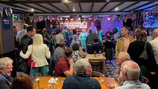 A crowded bar with wooden tables and a stage for live music. - The Bandstand (Nairn)