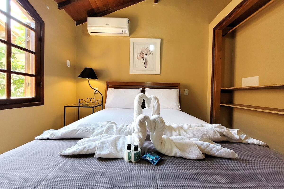 Habitación de hotel con cama, mesita de noche, lámpara, aire acondicionado y un cuadro en la pared.