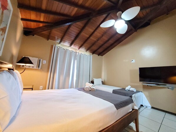 A hotel room with a wooden ceiling, a bed with white bedding, a flat-screen TV mounted on the wall, and a ceiling fan. - Pousada Canoas Buzios (Buzios)