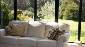 A white sofa with polka dot cushions, positioned in front of a large window with a view of a garden. - White Lodge B&B (Lewes)