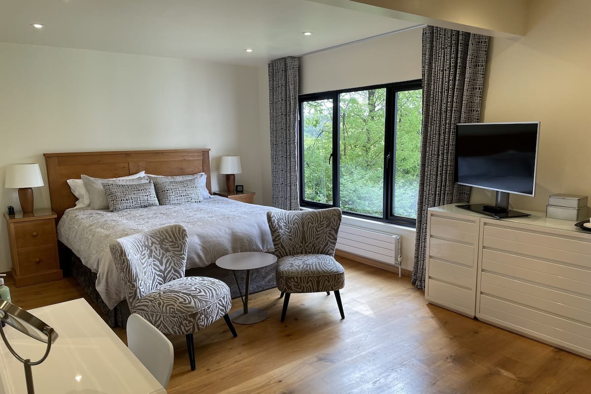 A bedroom with a large bed, two armchairs, a small table, a TV, and a dresser.