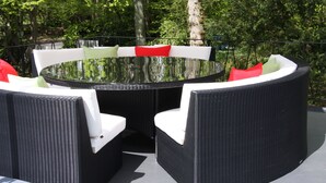 A round outdoor dining table with wicker chairs, surrounded by lush greenery. - White Lodge B&B (Lewes)