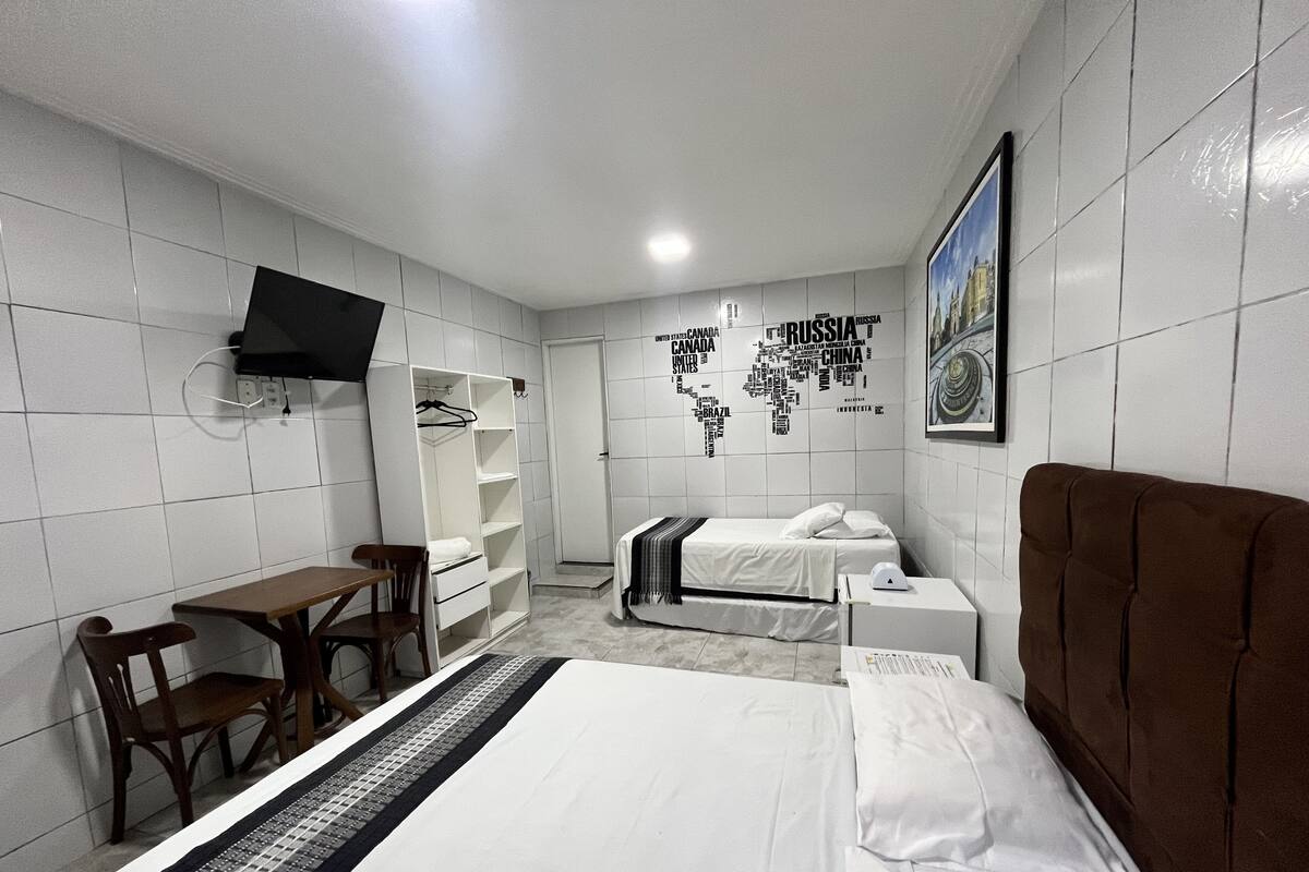 A hotel room with a bed, a desk, a chair, a wardrobe, and a world map on the wall.