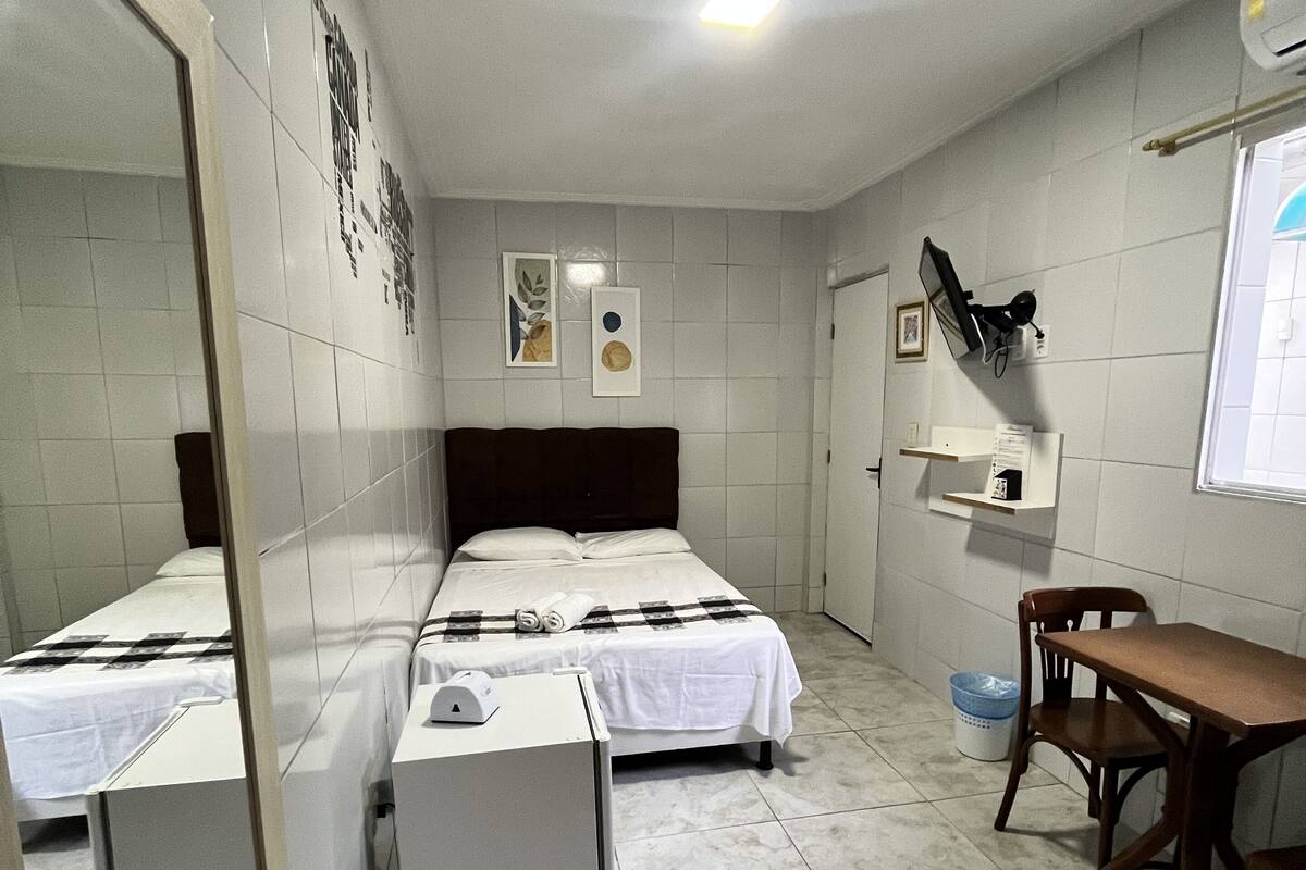 A hotel room with two single beds, a desk, a chair, a mirror, and a window.