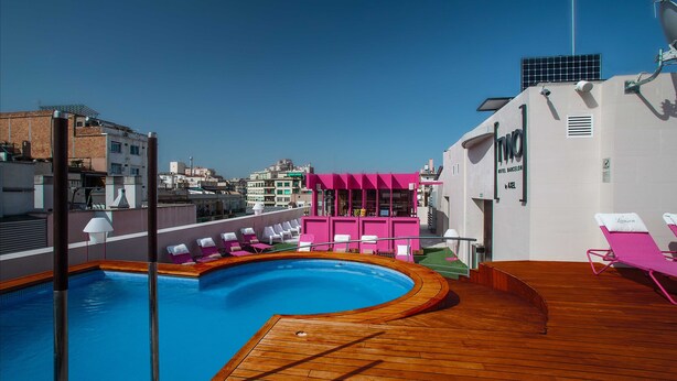 Un área de piscina en la azotea con una terraza de madera, sillas de descanso y una estructura rosa.