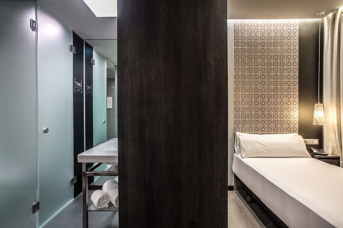 Una habitación de hotel con una cama, una mesita con toallas, un espejo y una pared con diseño.