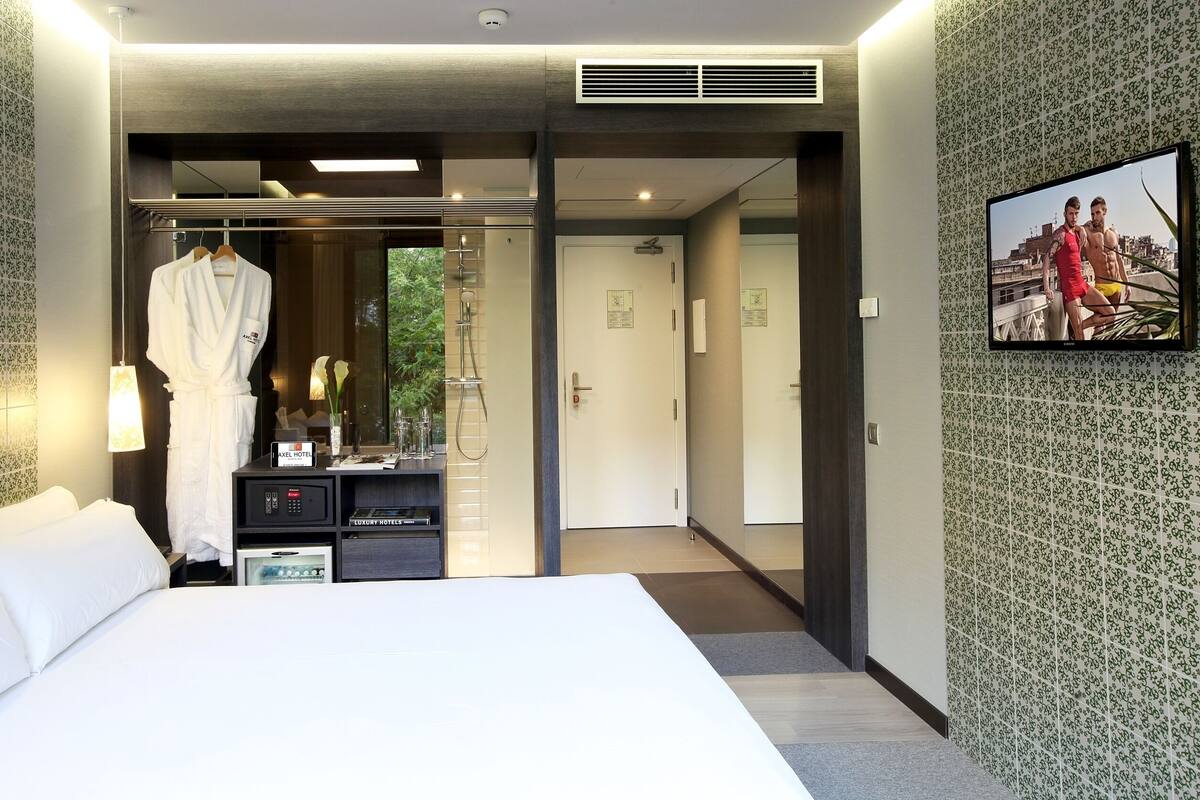 Una habitación de hotel moderna con una cama grande, un vestidor, zona de ducha y un televisor en la pared.