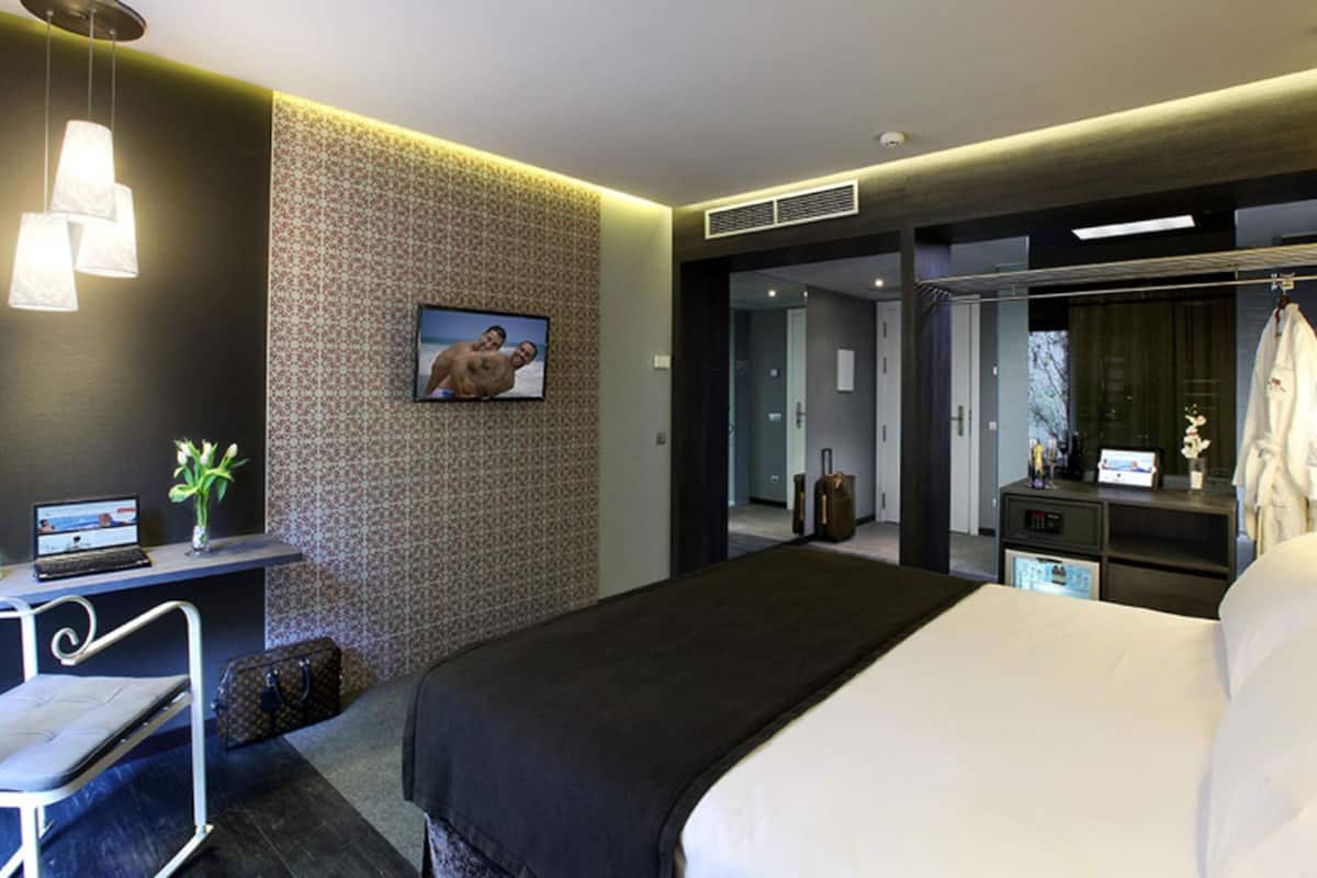 Una habitación de hotel moderna con una cama grande, un escritorio con una computadora portátil, un televisor y un armario.