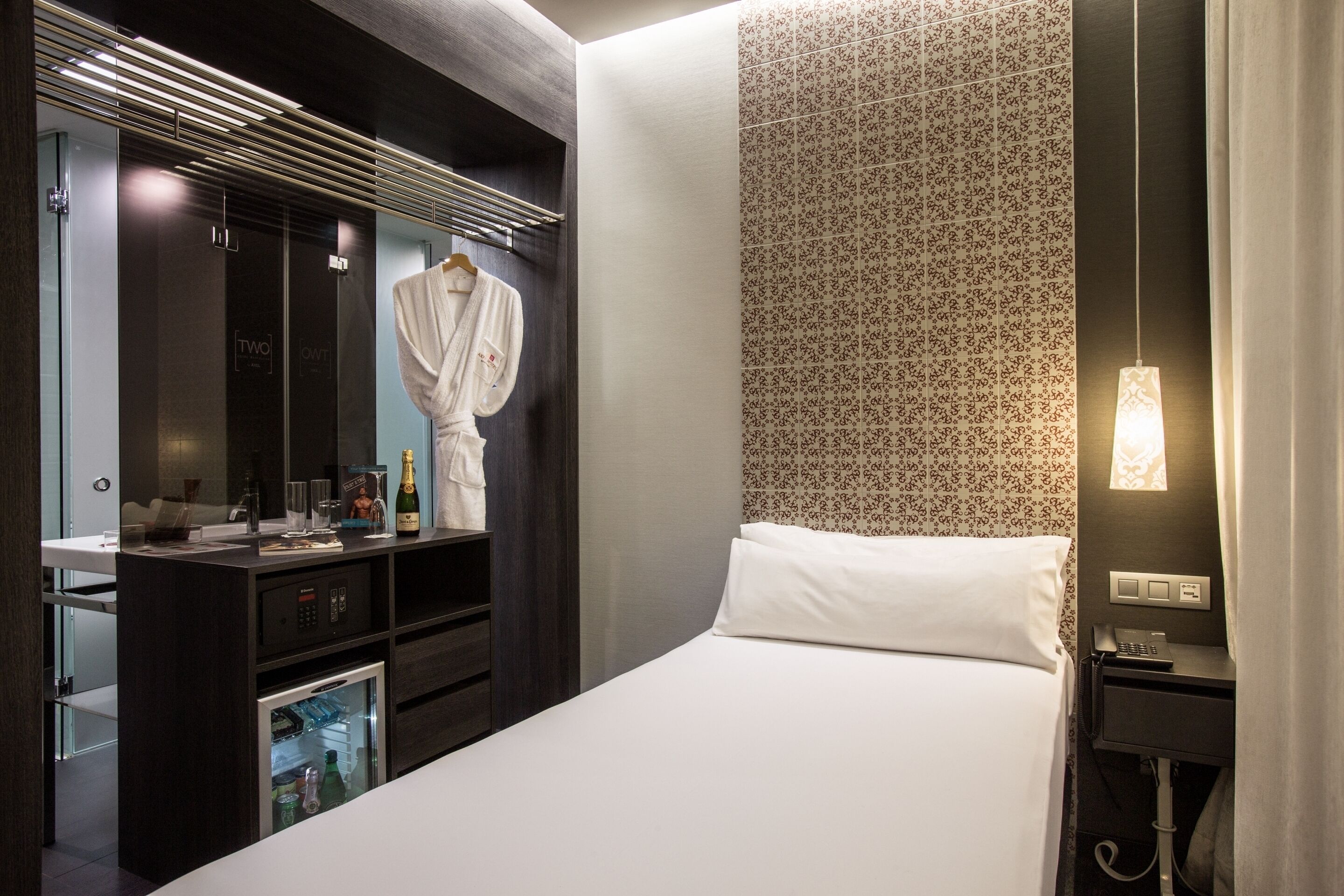 Una habitación de hotel moderna con una cama, un tocador con espejo, un minibar y una zona de ducha.