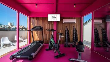 Un gimnasio moderno con interior rosa, una cinta de correr, una bicicleta estática y máquinas de pesas.