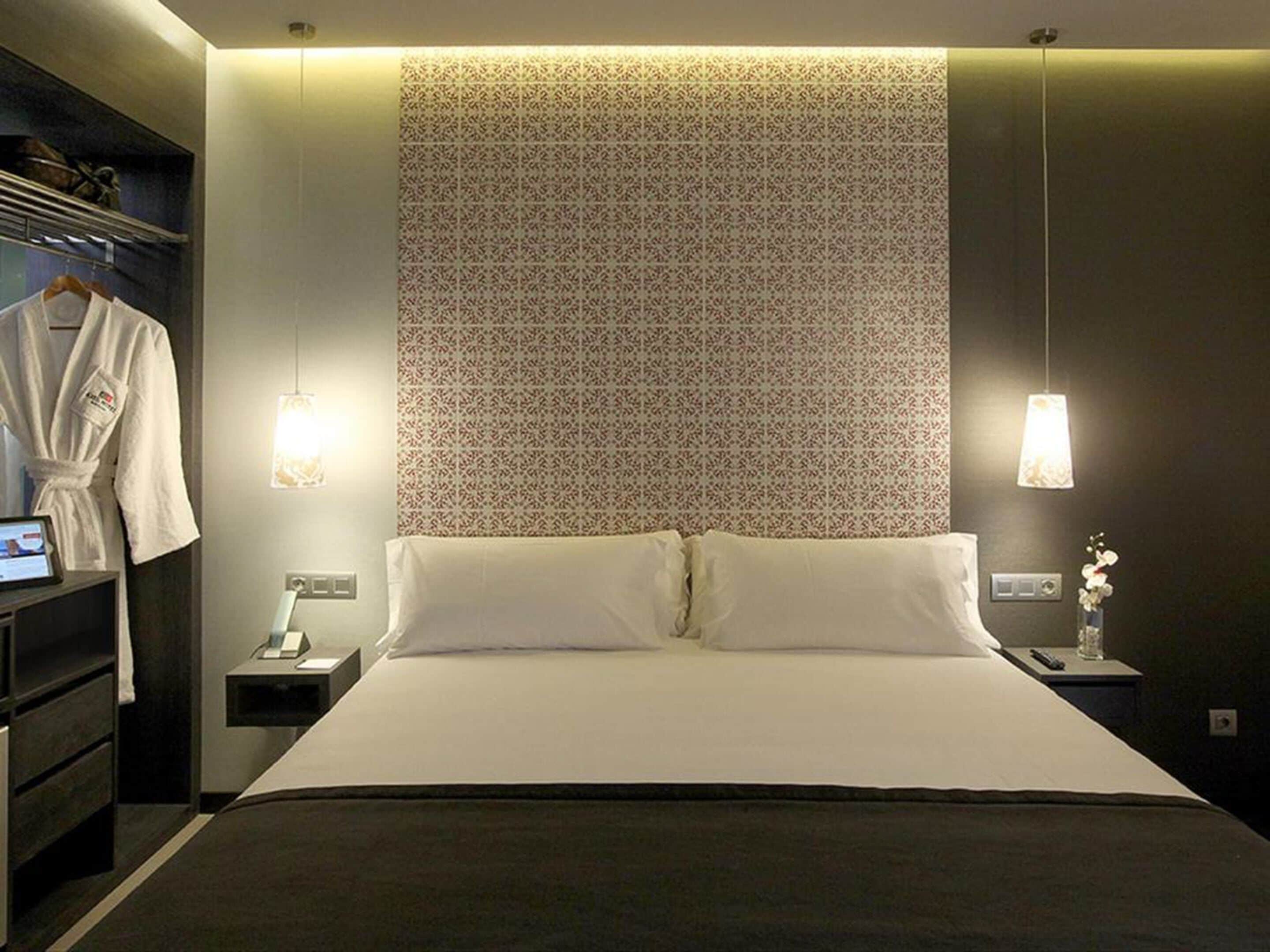 A modern hotel room with a large bed, a robe hanging on a rack, and two bedside tables with lamps.