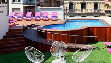A rooftop pool area with a wooden deck, a swimming pool, and several lounge chairs.
