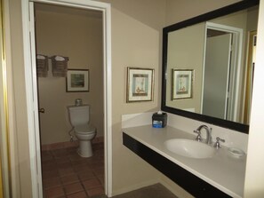 A bathroom with a toilet, sink, and mirror. There are framed pictures on the wall.