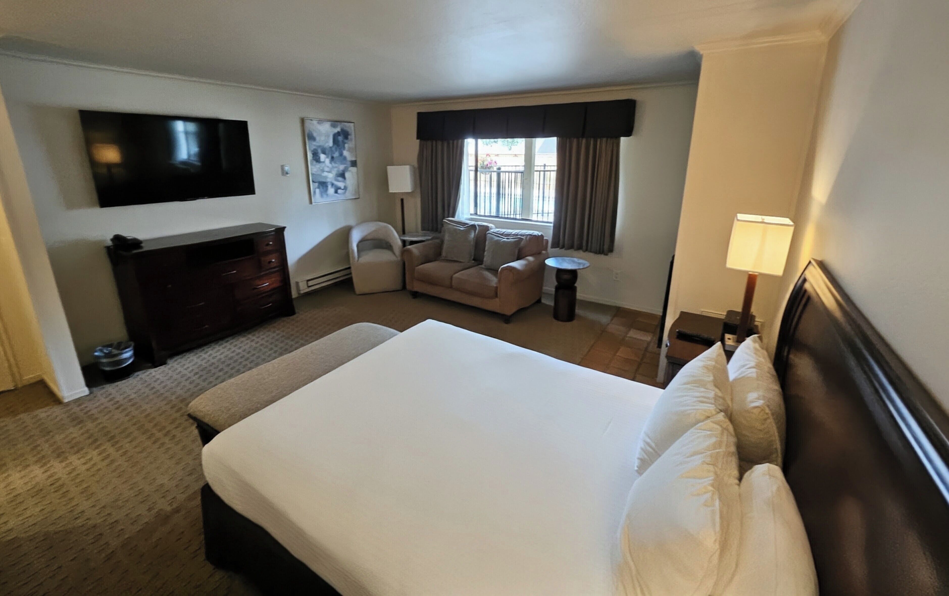 Habitación de hotel con una cama grande, televisión, sofá, una mesita y ventana con cortinas.