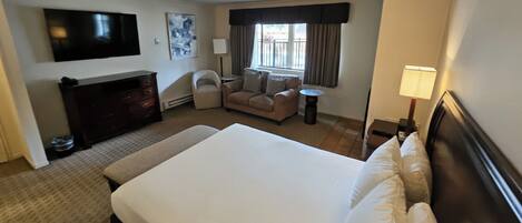 Habitación de hotel con una cama grande, televisión, sofá, una mesita y ventana con cortinas.