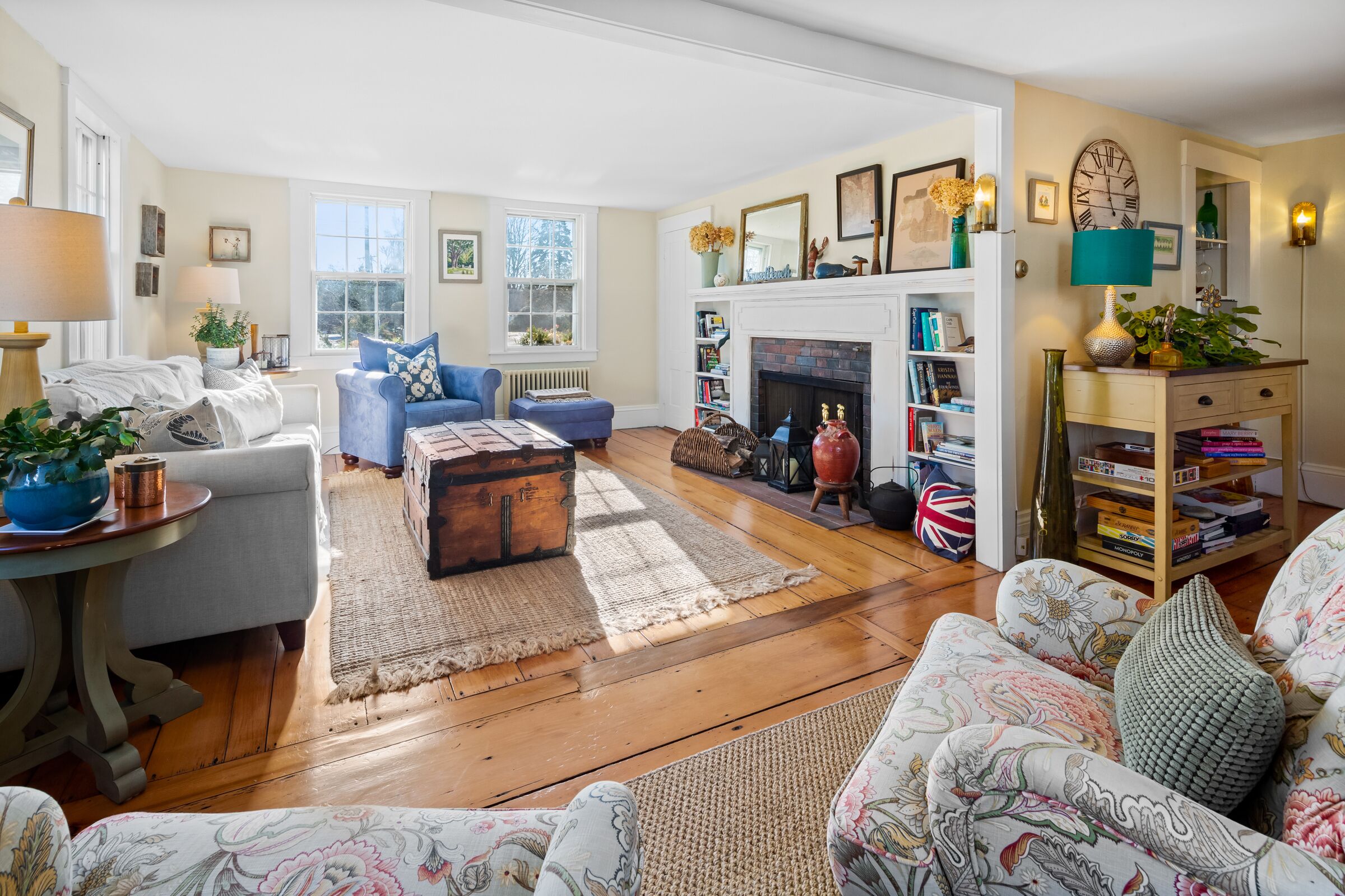 A cozy living room with a fireplace, a blue armchair, a patterned sofa, and a bookshelf.