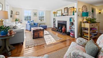 A cozy living room with a fireplace, a blue armchair, a patterned sofa, and a bookshelf.