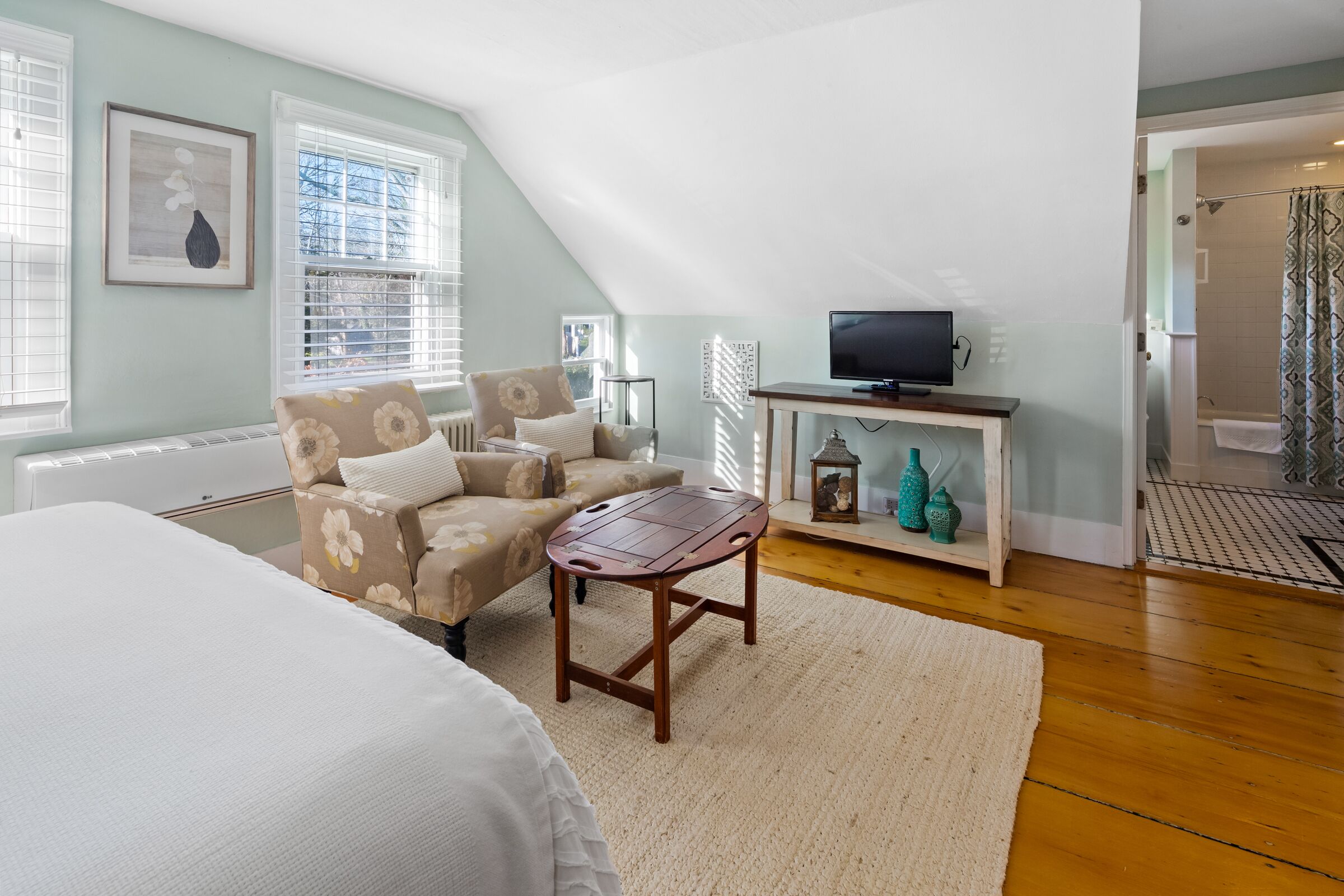 Una habitación acogedora con cama, sofá, una mesita de madera, televisor y un baño visible a través de una puerta abierta.