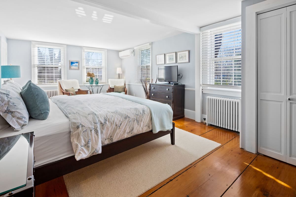 A bedroom with a bed, a dresser, a TV, and a window with blinds.