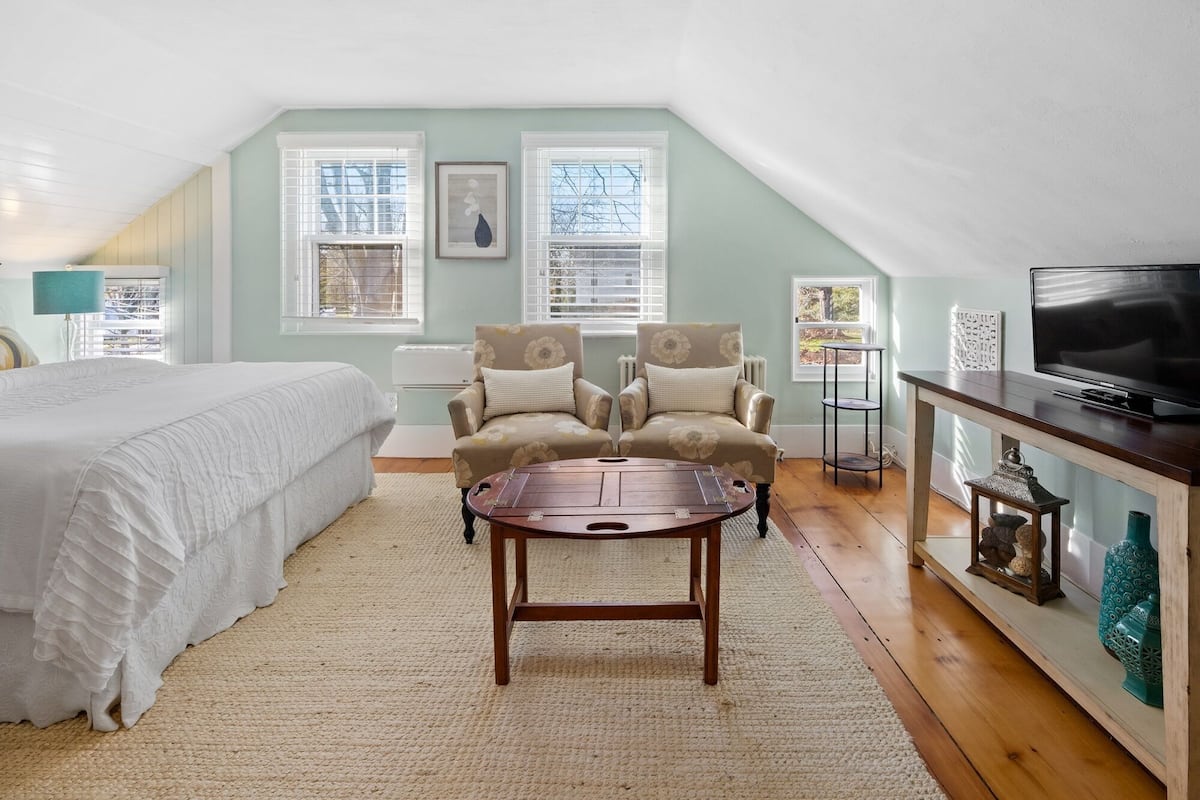 A bedroom with a bed, a desk, a chair, a TV, and a window.