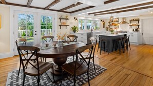 A spacious kitchen with wooden beams, a large island, and a dining area with a round table and chairs. - The Parsonage Inn (Orleans)