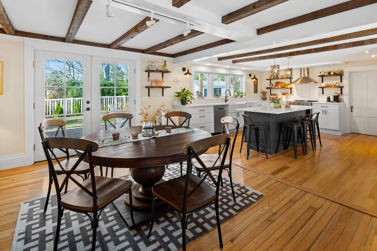 A spacious kitchen with wooden beams, a large island, and a dining area with a round table and chairs.