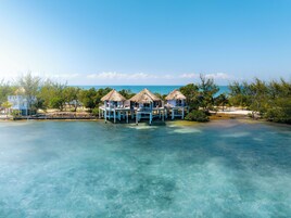 Bungalows sobre el agua con techos de paja, unidos por una pasarela de madera, con vistas a aguas turquesas cristalinas.