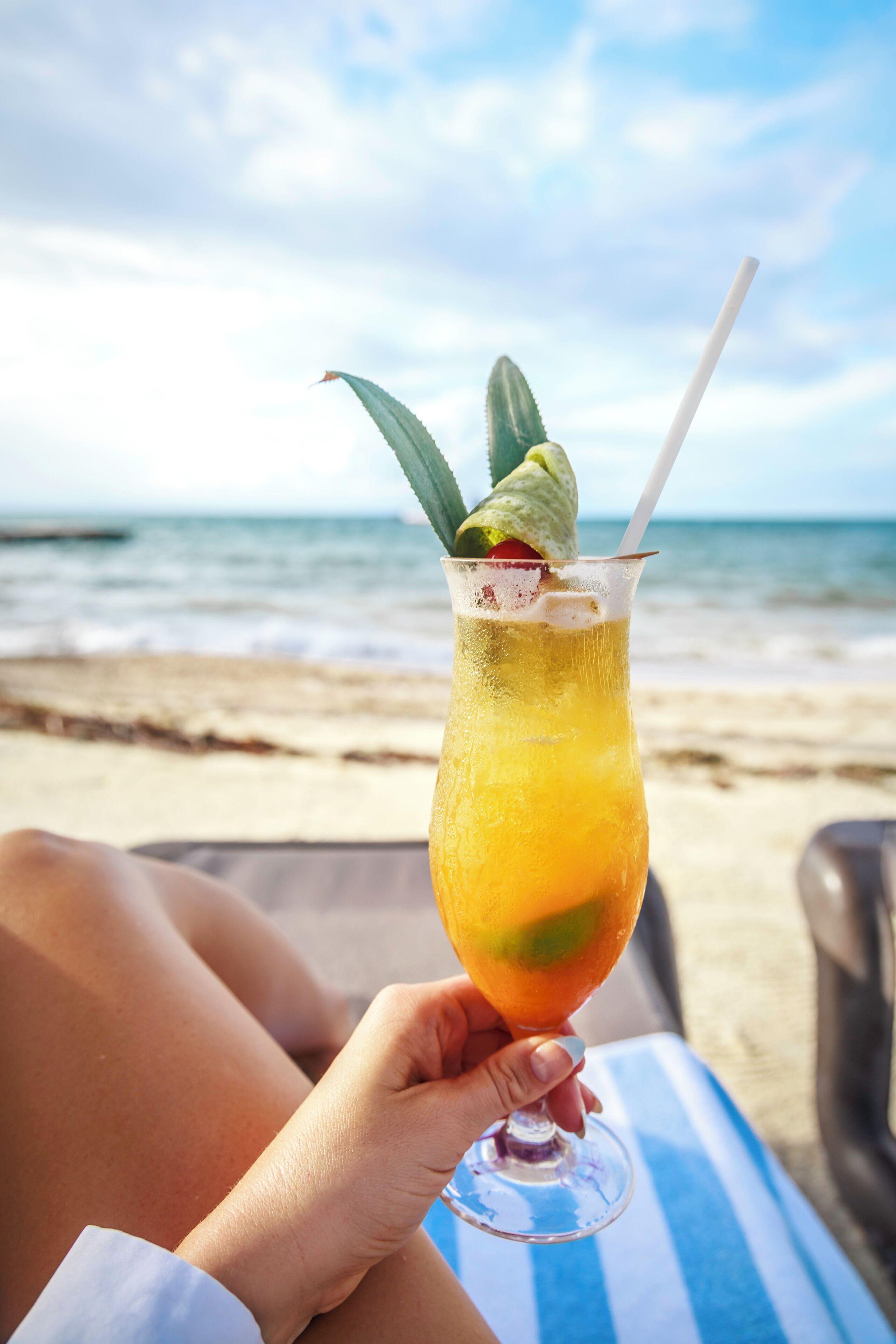 A person holding a cocktail on a beach with a clear view of the ocean.