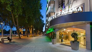 A hotel entrance with a modern design, a visible parking sign, and a bench on the sidewalk.