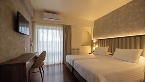 A hotel room with a bed, a desk, a chair, a TV, and a window with curtains.