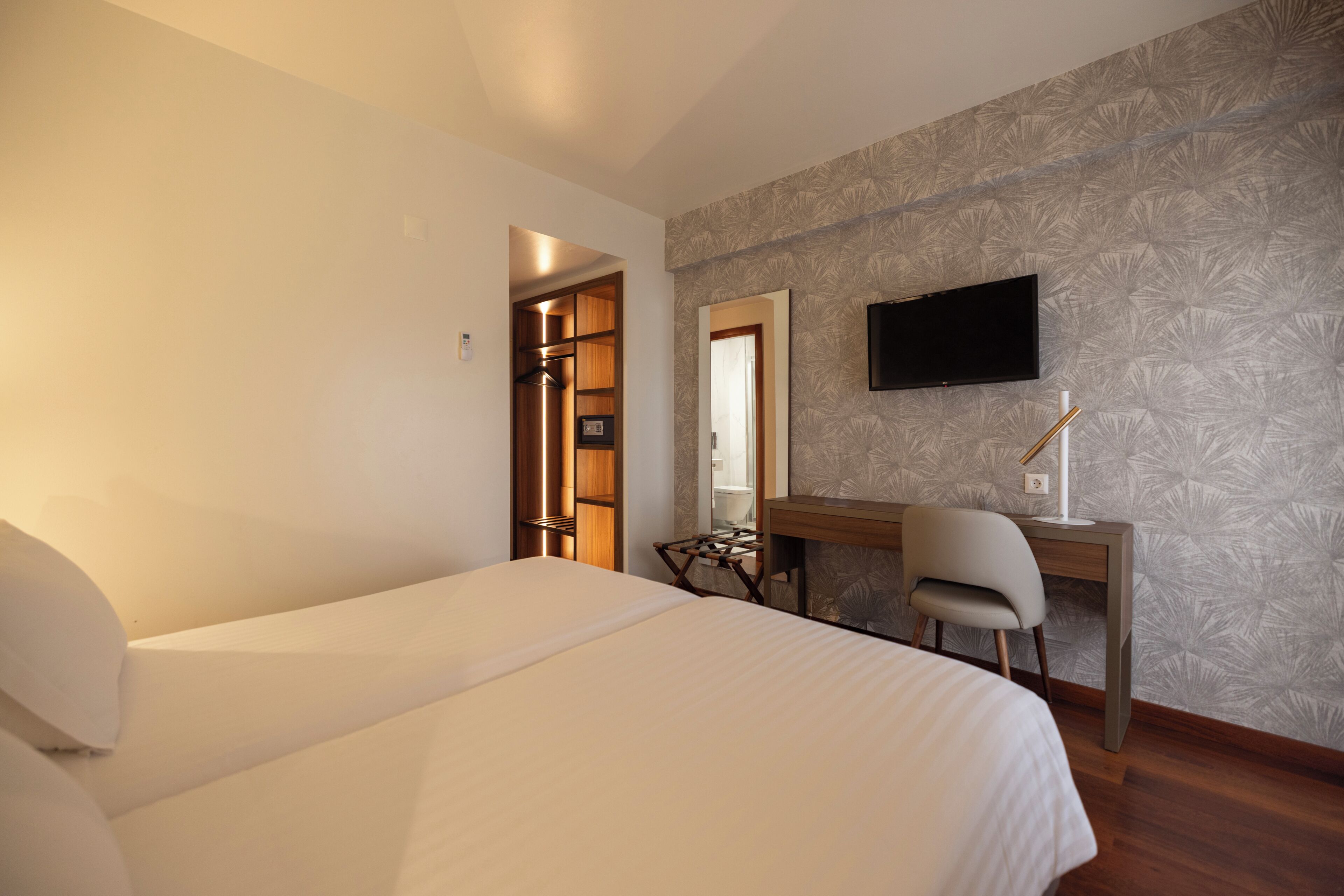 A hotel room with a bed, desk, chair, and a television on the wall.