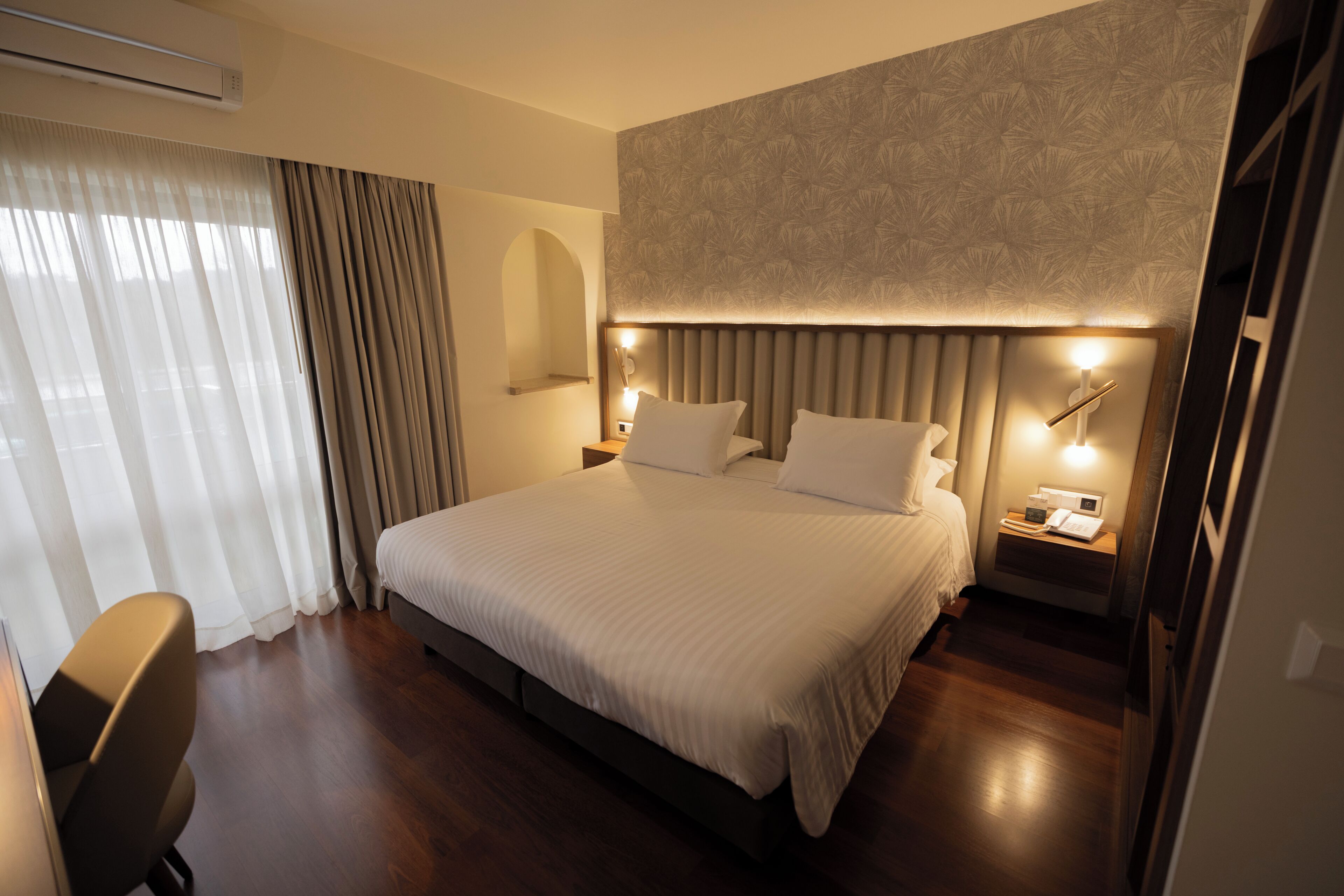 A modern hotel room with a large bed, bedside tables, a desk, and a chair.